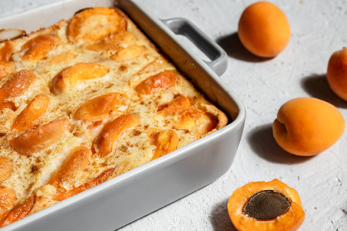 Clafoutis avec abricot - tarte d'été dans un plat de boulangerie et abricots frais sur la table claire