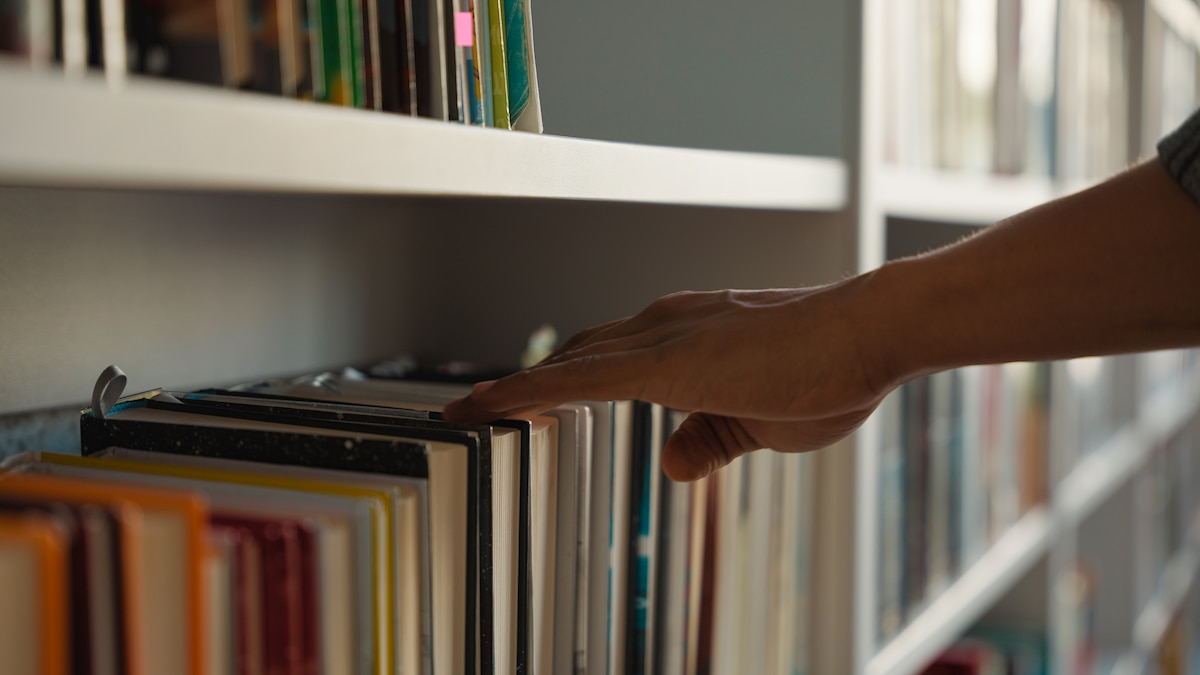 Main d'homme choisissant un livre dans une étagère.