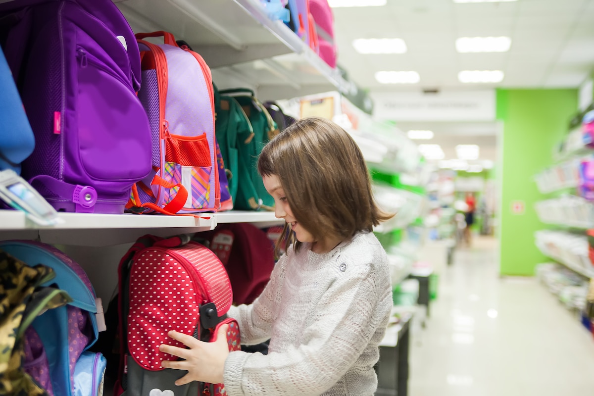 jeune fille regardant un cartable dans un rayon de supermarché