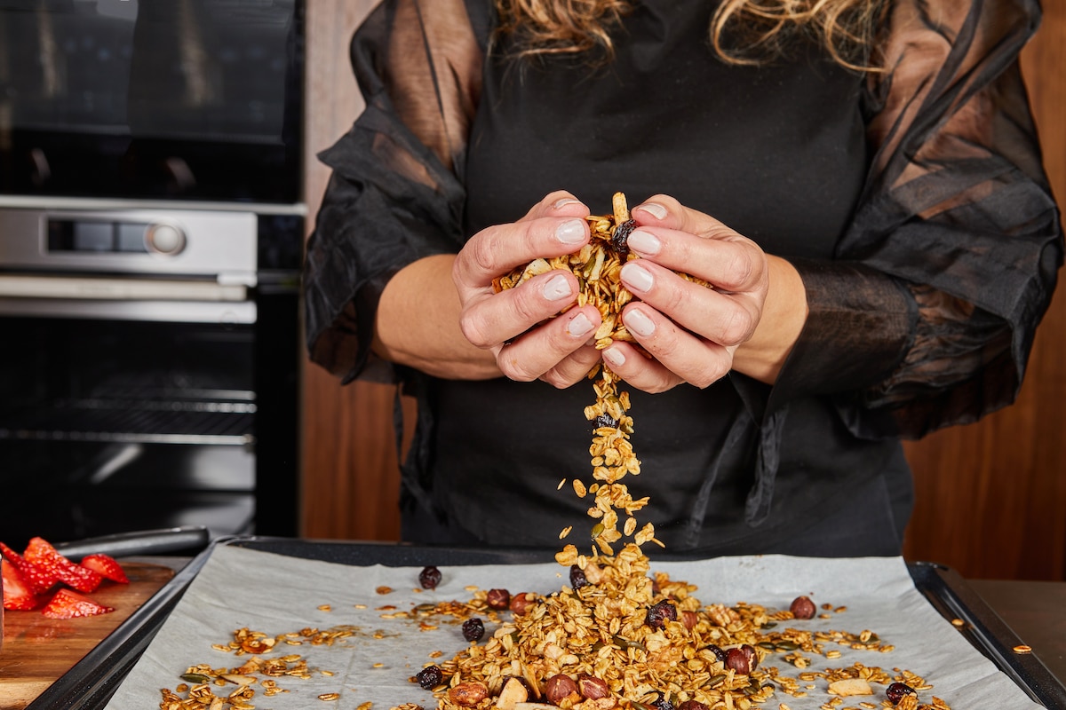 Une personne utilise ses mains pour mélanger délicatement le granola fraîchement cuit sur un plateau, assurant une texture et une distribution uniformes des ingrédients