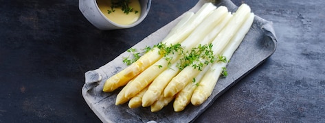Asperges blanches glacées avec sauce hollandaise et cresson servie en gros plan sur un plateau design
