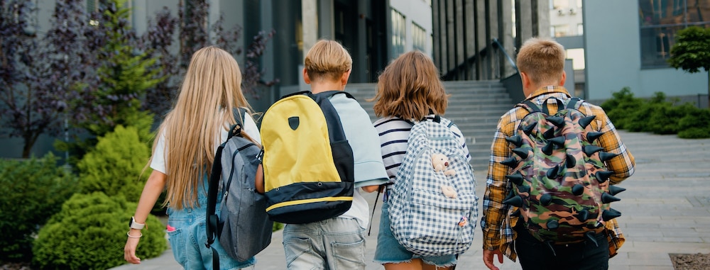 4 enfants de dos marchant avec leur cartables sur le dos