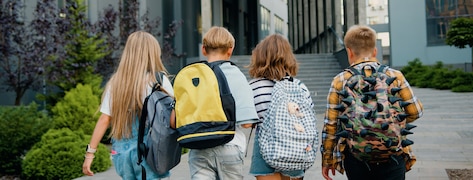 4 enfants de dos marchant avec leur cartables sur le dos