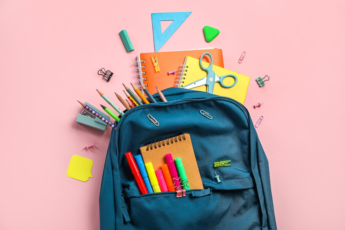 Fournitures scolaires déposées près d'un cartable.