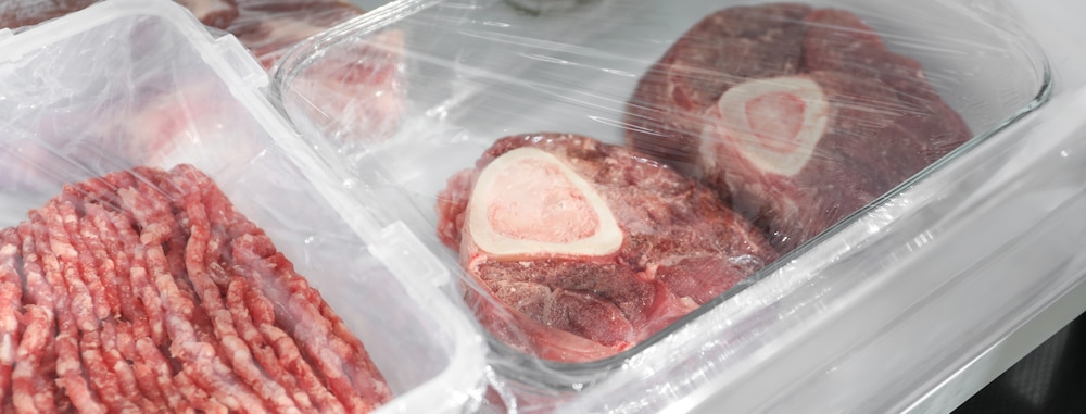 Steaks de boeuf congelés et viande hachée dans des contenants sur l'étagère du réfrigérateur, en gros plan