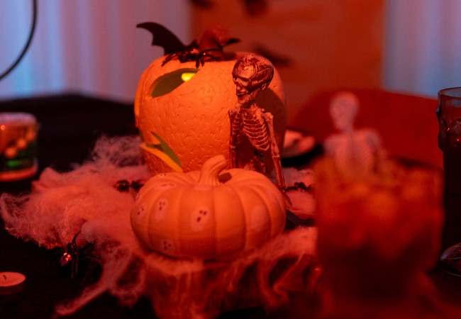 Table décorée pour Halloween avec des citrouilles, un squelette et des toiles d’araignée.