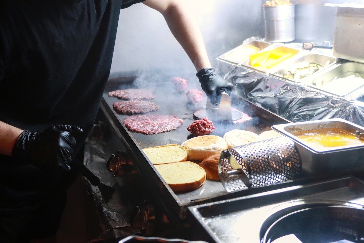 Commis de cuisine préparant un smash burger dans une cuisine de restaurant.