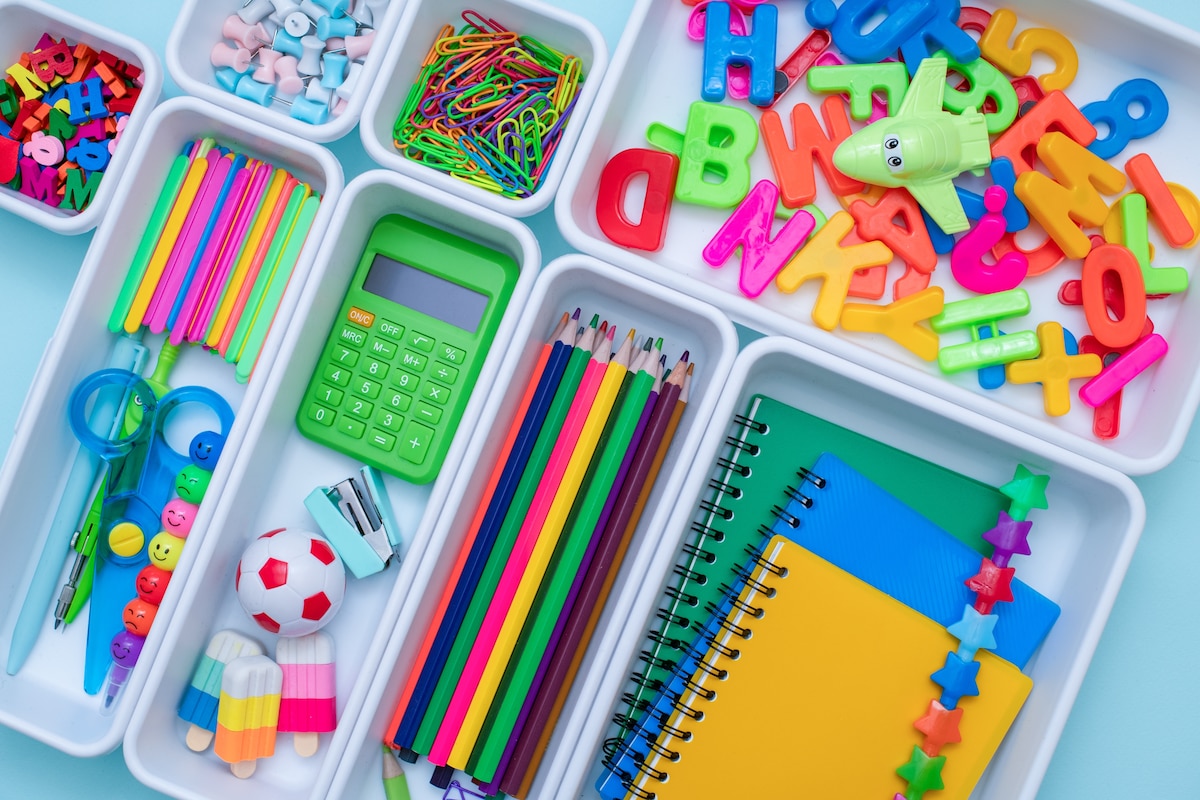 Fournitures scolaires colorées rangées dans des petites boîtes blanches.