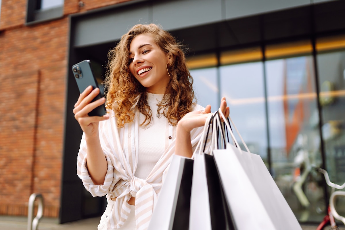 Jeune femme regardant son téléphone en tenant des sacs de vêtements