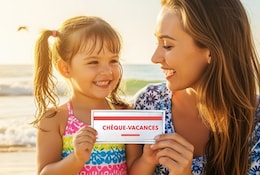 Une mère souriante et sa fille tiennent un chèque-vacances à la plage.