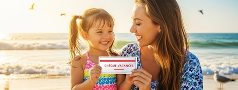 Une mère souriante et sa fille tiennent un chèque-vacances à la plage.