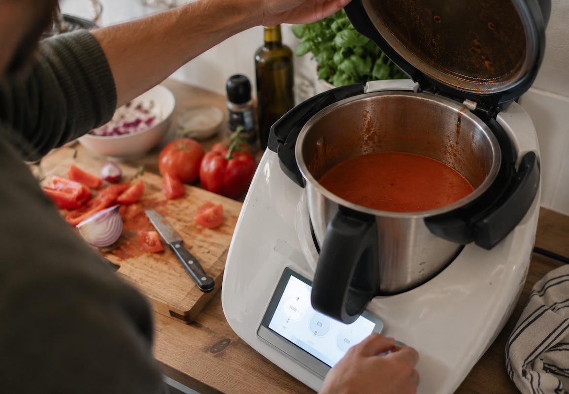 Une personne prépare une soupe de tomates rouge dans un robot cuiseur, sur un plan de travail avec des légumes frais.
