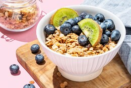  Granola ou muesli au four dans un bol avec kiwi et bleuets sur une planche en bois sur fond rose.