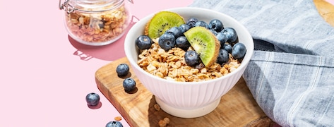  Granola ou muesli au four dans un bol avec kiwi et bleuets sur une planche en bois sur fond rose.