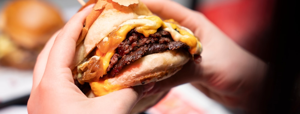 Mains tenant un juteux burger double smash avec cheddar fondu et oignons.
