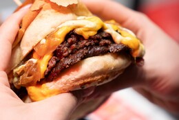 Mains tenant un juteux burger double smash avec cheddar fondu et oignons.