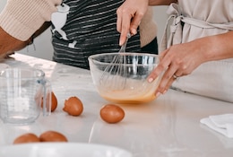 2 personnes cuisinent en battant des œufs dans un grand bol.