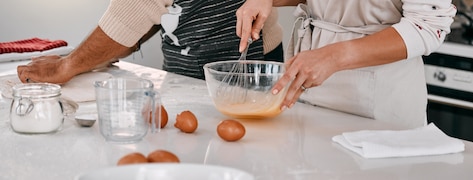 2 personnes cuisinent en battant des œufs dans un grand bol.
