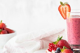Verre de smoothie aux fruits rouges avec des fruits rouges disposés autour.