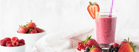 Verre de smoothie aux fruits rouges avec des fruits rouges disposés autour.